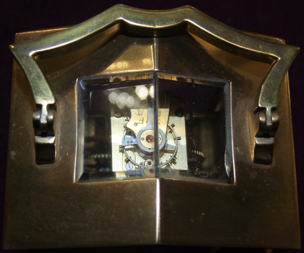 An antique polished brass Georgian revival carriage clock featuring a white dial with Roman numerals, a top carrying handle, and an accompanying winding key. View VI
