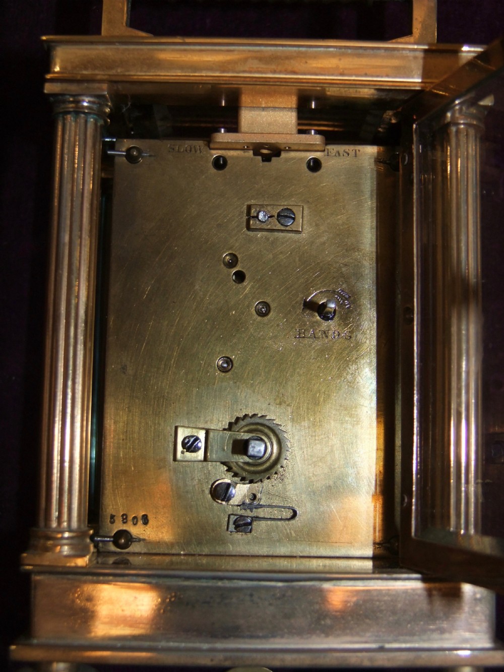 A gilt bronze architectural carriage clock featuring side fluted columns, a reeded carrying handle, compressed bun feet, and a white enamel dial with Roman numerals. View VI