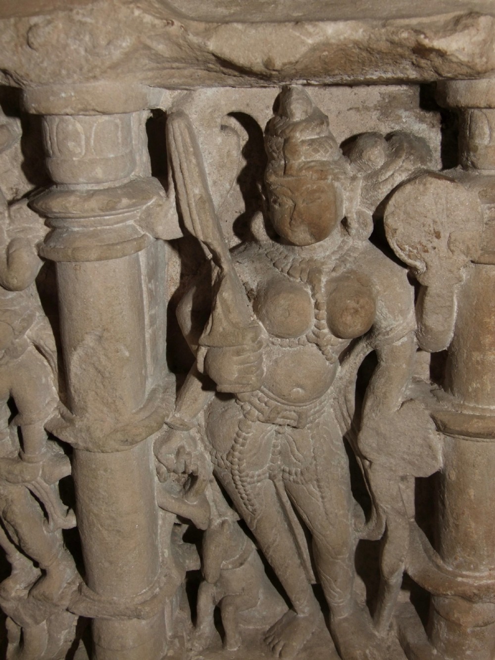 A carved beige sandstone relief fragment from 11th century India depicting the Hindu deity Parvati flanked by decorative columns and smaller attendant figures. View III