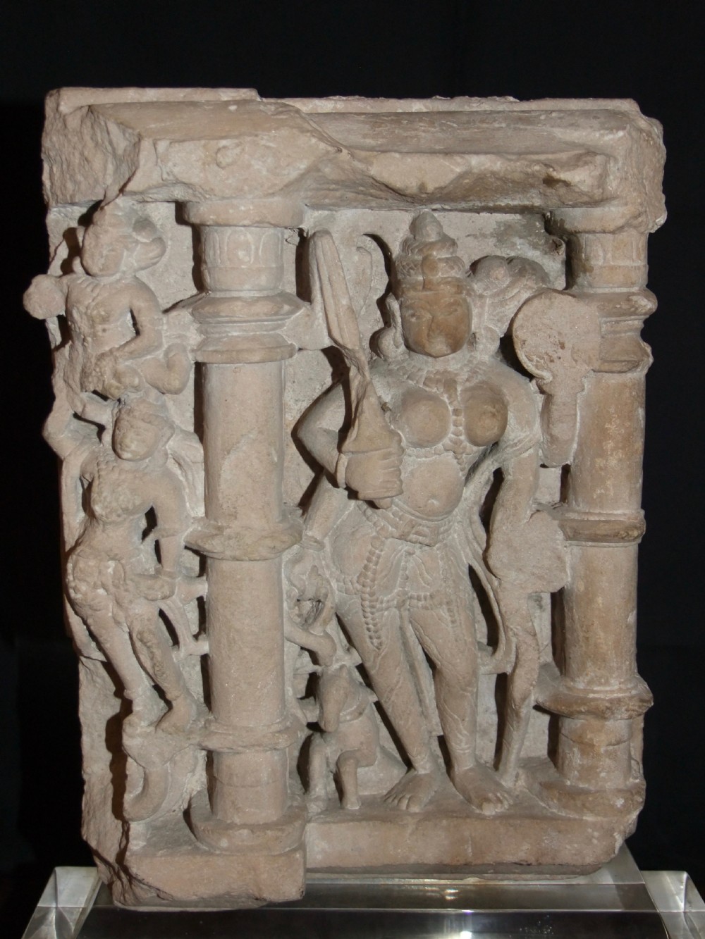 A carved beige sandstone relief fragment from 11th century India depicting the Hindu deity Parvati flanked by decorative columns and smaller attendant figures. View VI