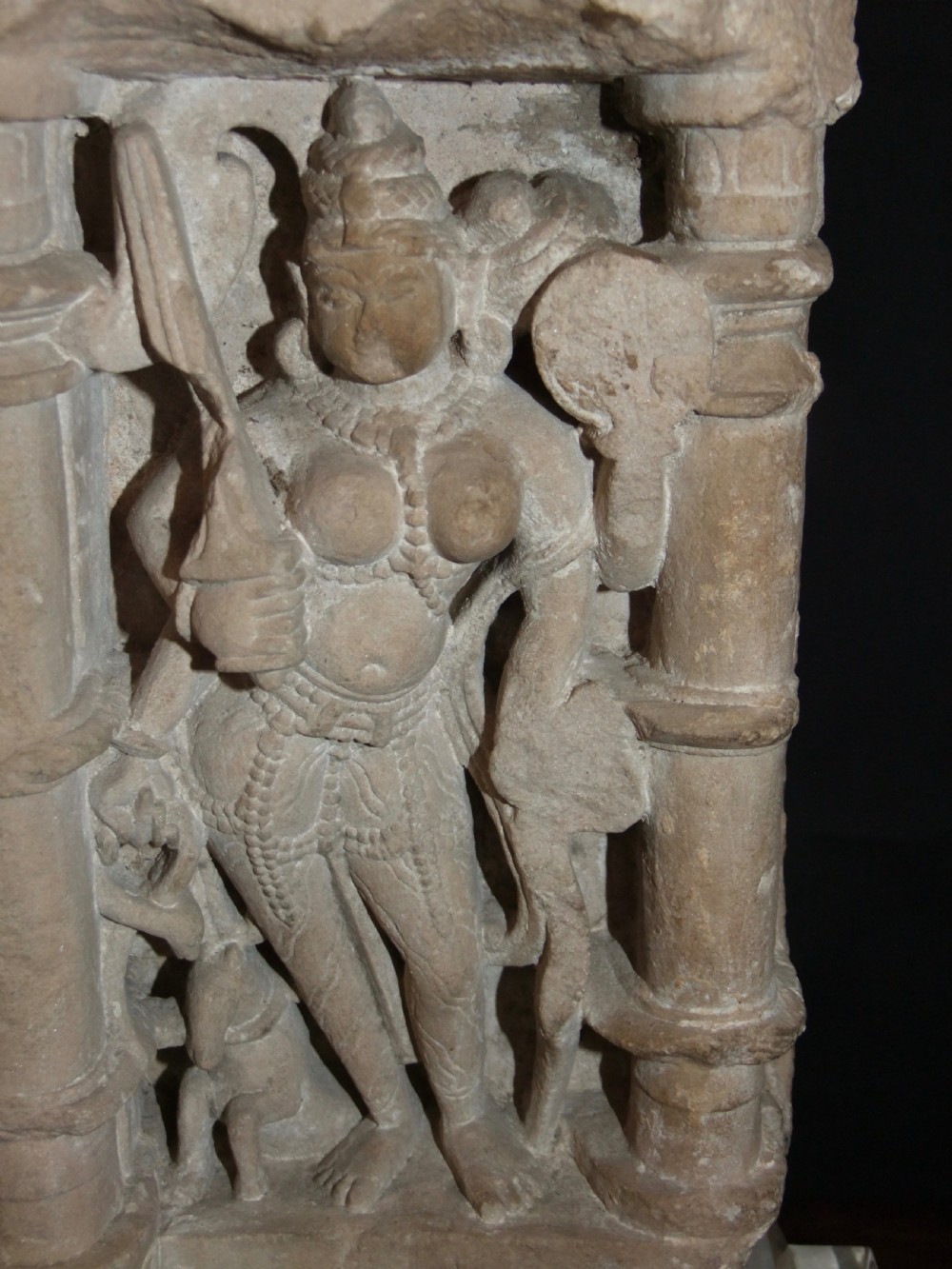 A carved beige sandstone relief fragment from 11th century India depicting the Hindu deity Parvati flanked by decorative columns and smaller attendant figures. View VII