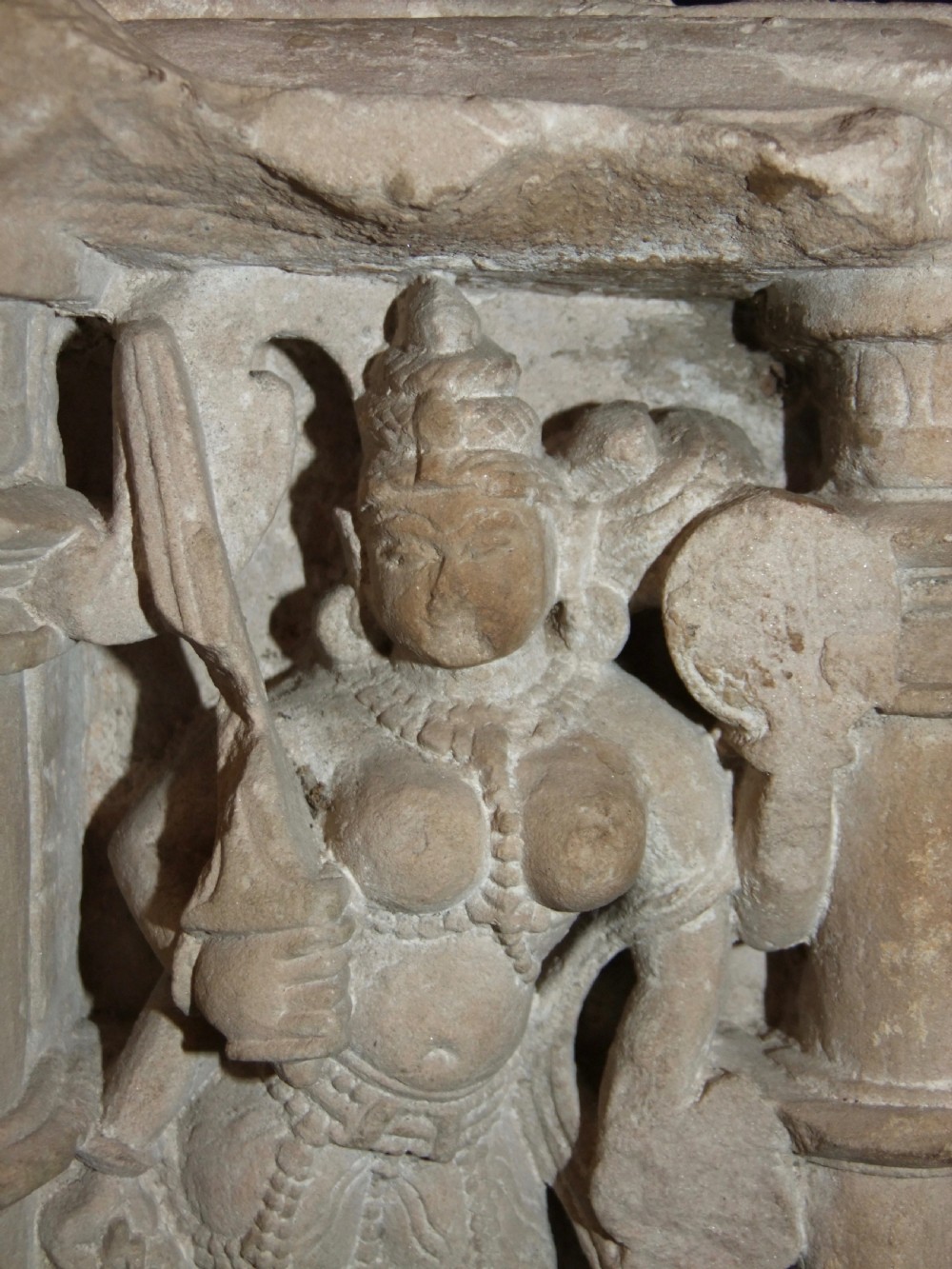 A carved beige sandstone relief fragment from 11th century India depicting the Hindu deity Parvati flanked by decorative columns and smaller attendant figures. View VIII