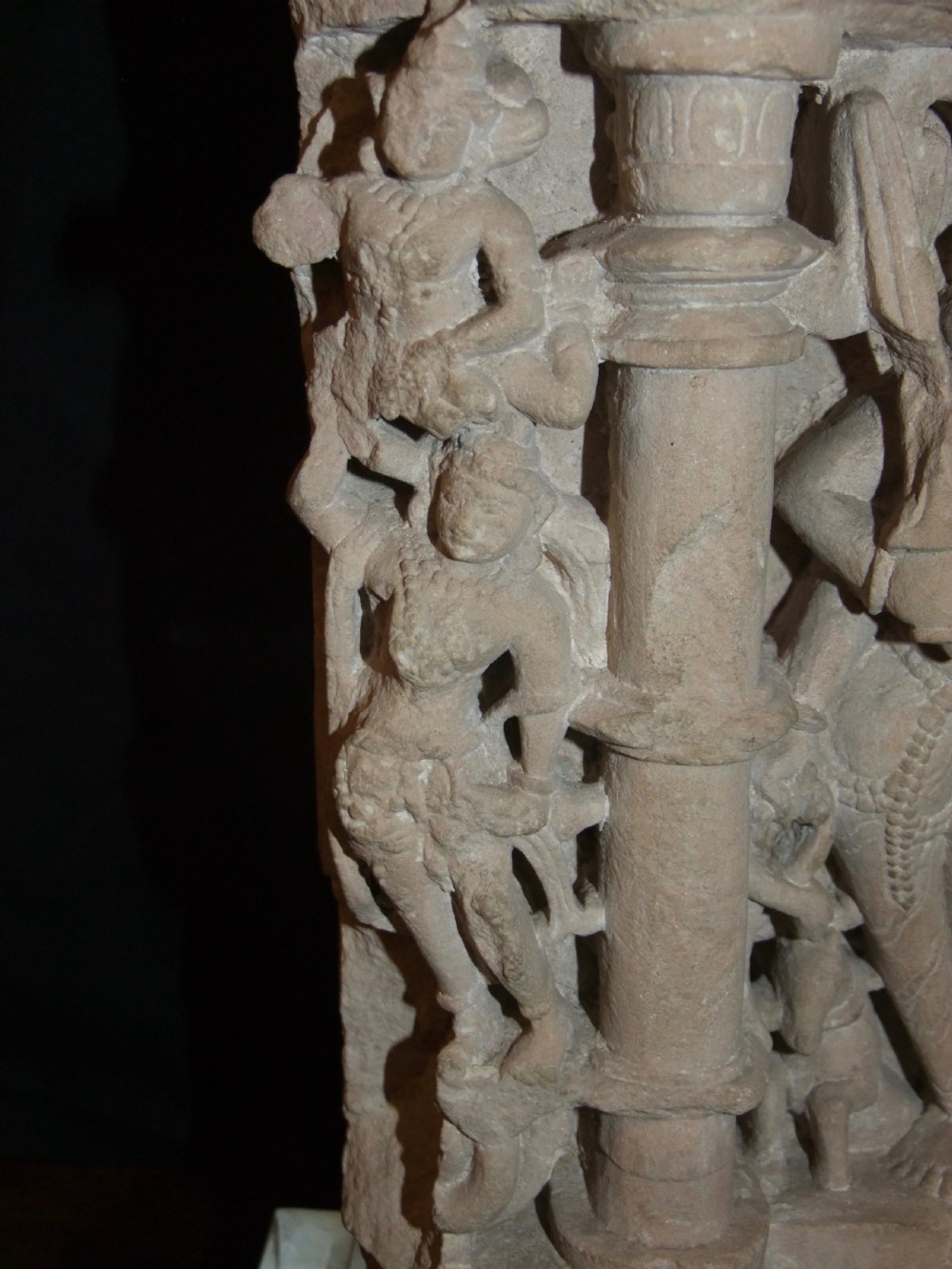 A carved beige sandstone relief fragment from 11th century India depicting the Hindu deity Parvati flanked by decorative columns and smaller attendant figures. View IX