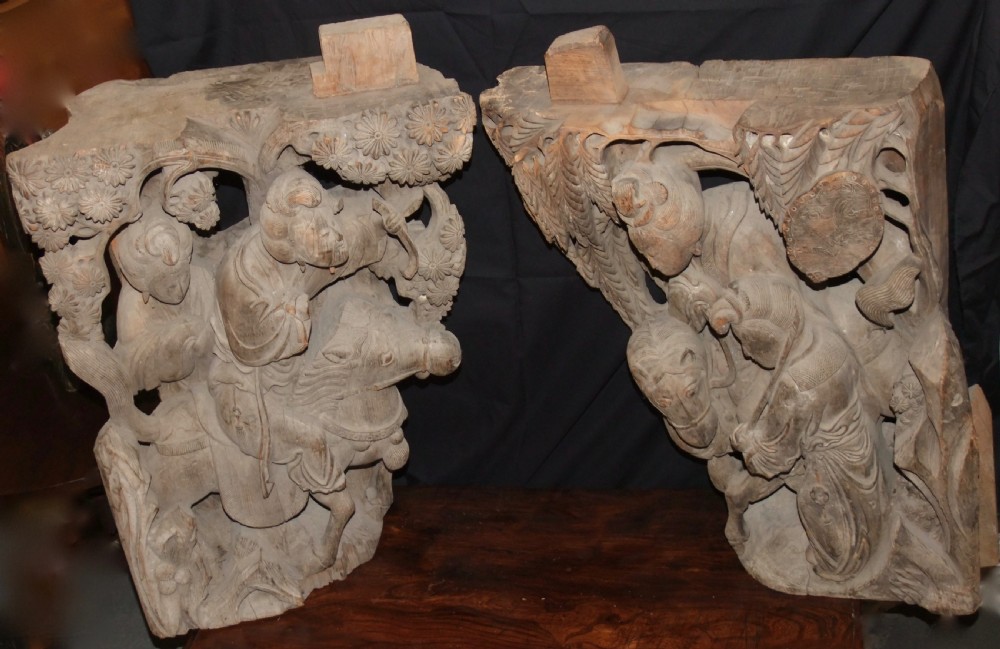 A pair of deeply carved natural timber architectural corbels depicting figures mounted on horses amidst floral motifs.