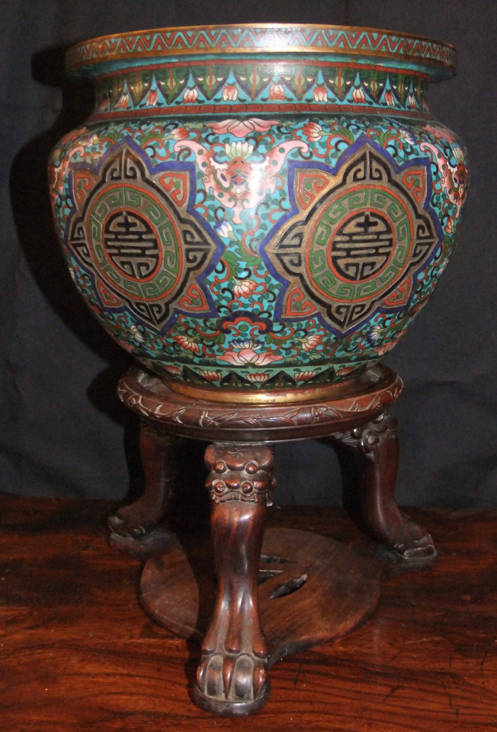 A large Chinese cloisonne enamel jardiniere with floral scrollwork and longevity motifs resting on a dark carved wood stand. View II