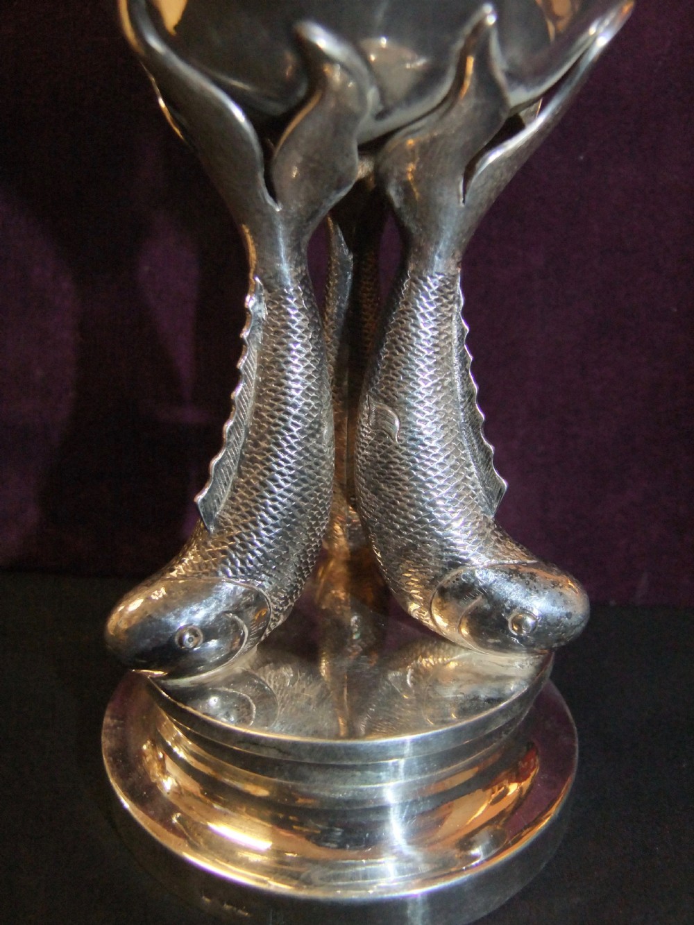 A polished silver goblet featuring a plain round bowl supported by three cast koi carp fish forming the stem above a stepped circular base. View II