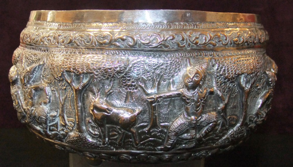 A 19th-century Burmese footed silver bowl featuring high-relief repousse decoration depicting figures, animals, and trees.