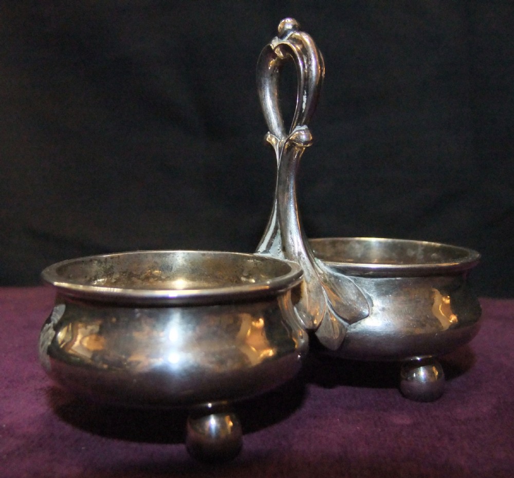 A 19th-century silver double salt cellar featuring twin circular bowls, spherical ball feet, and a central elevated looped handle with leaf detailing. View II