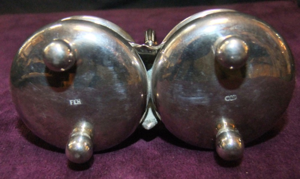 A 19th-century silver double salt cellar featuring twin circular bowls, spherical ball feet, and a central elevated looped handle with leaf detailing. View VI