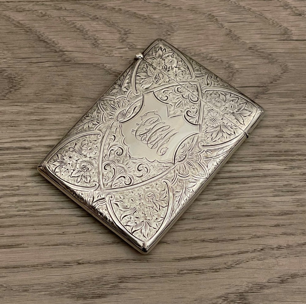 An Edwardian sterling silver calling card case featuring detailed foliate floral engraving and a central monogram cartouche.