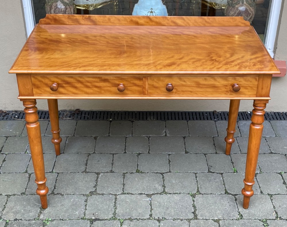 A Victorian satin birch side table featuring a low rear gallery, two front drawers with turned wooden knobs, and four turned tapered legs.