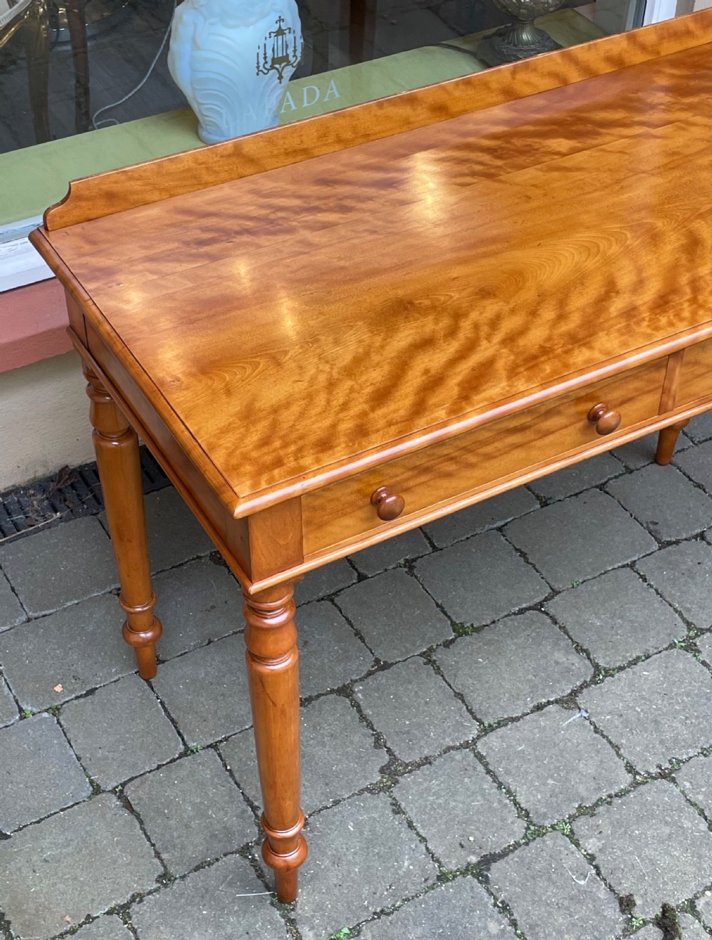 A Victorian satin birch side table featuring a low rear gallery, two front drawers with turned wooden knobs, and four turned tapered legs. View II