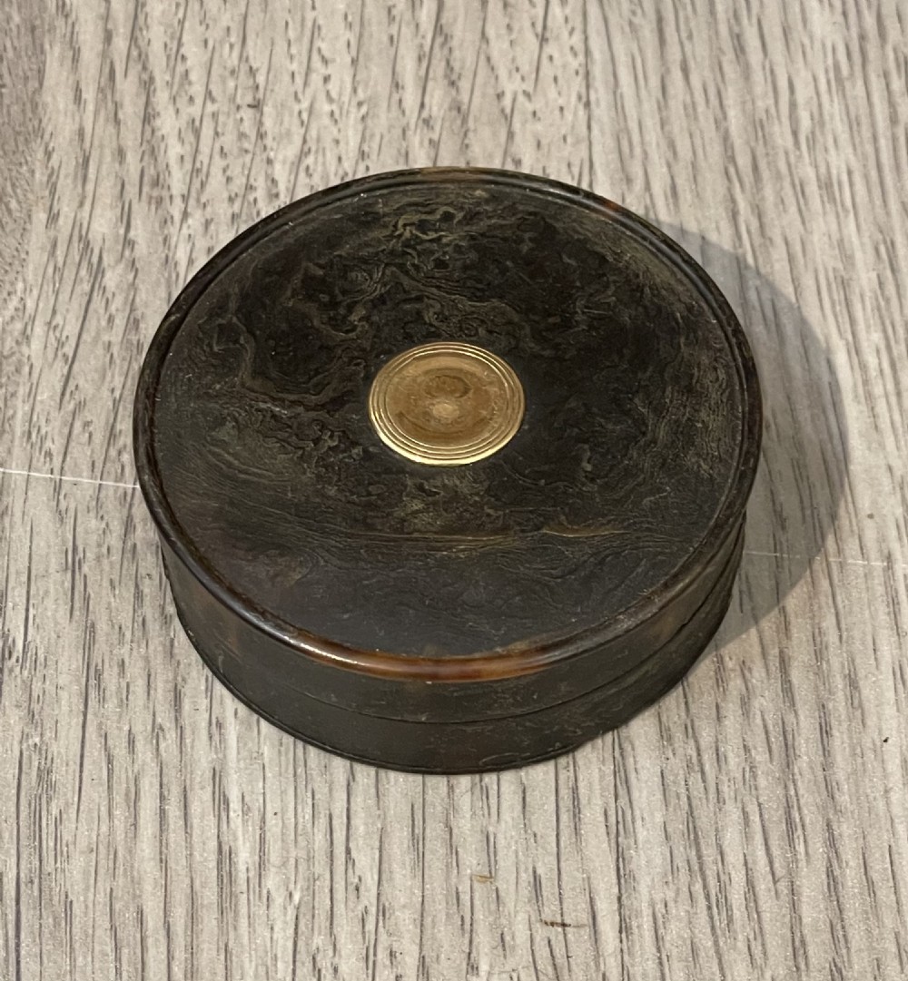 A small circular dark brown tortoiseshell snuff box with a central gold medallion inlay. View II