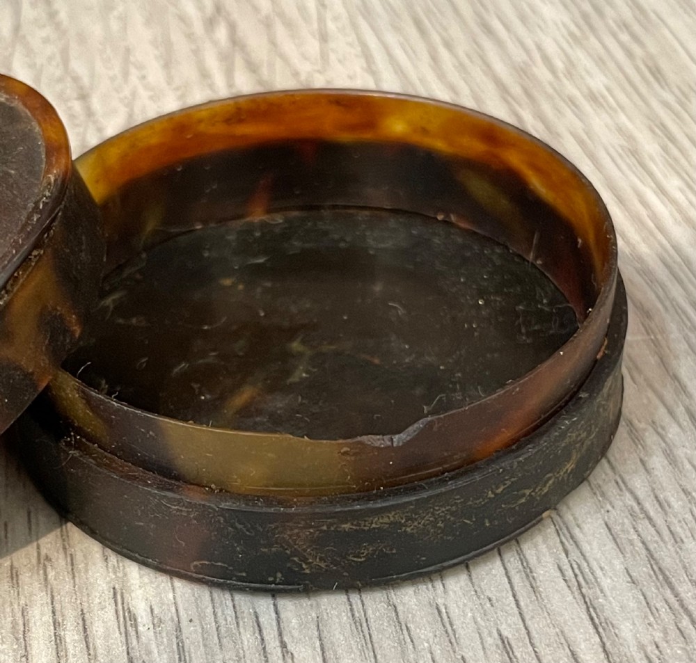 A small circular dark brown tortoiseshell snuff box with a central gold medallion inlay. View III