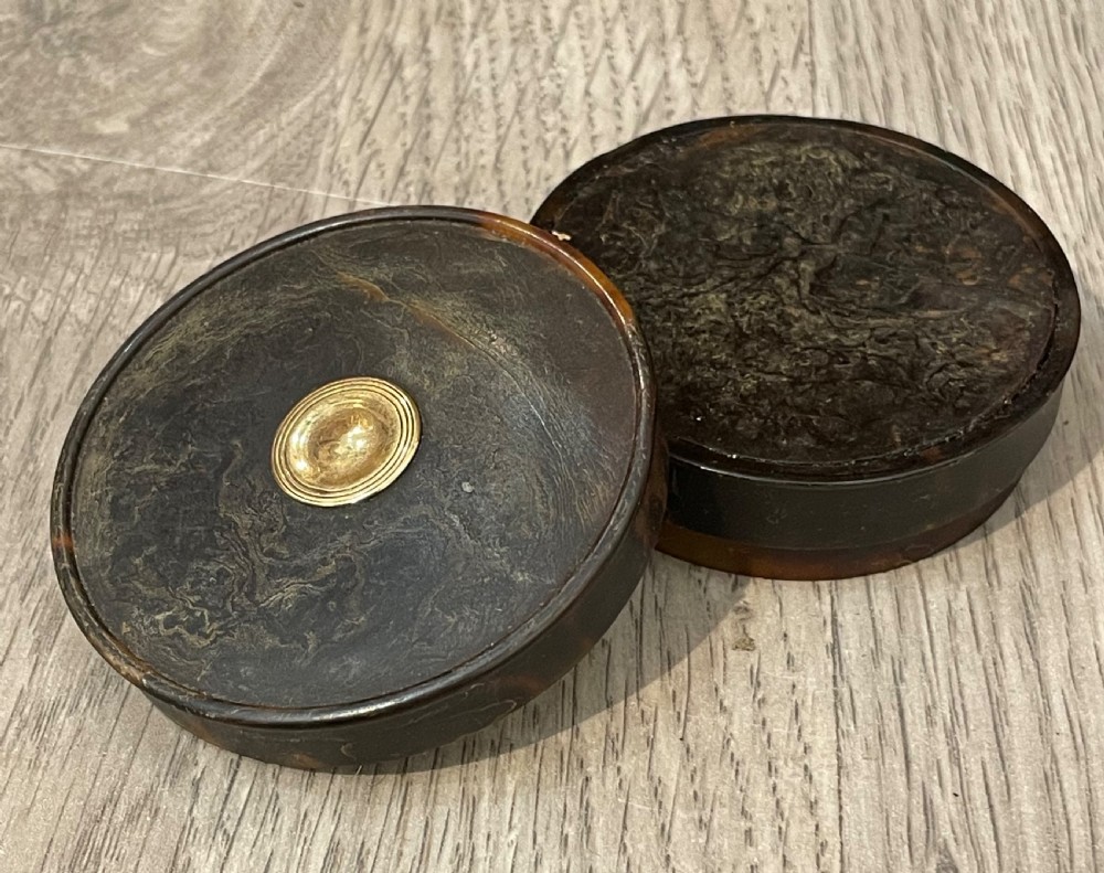 A small circular dark brown tortoiseshell snuff box with a central gold medallion inlay. View V