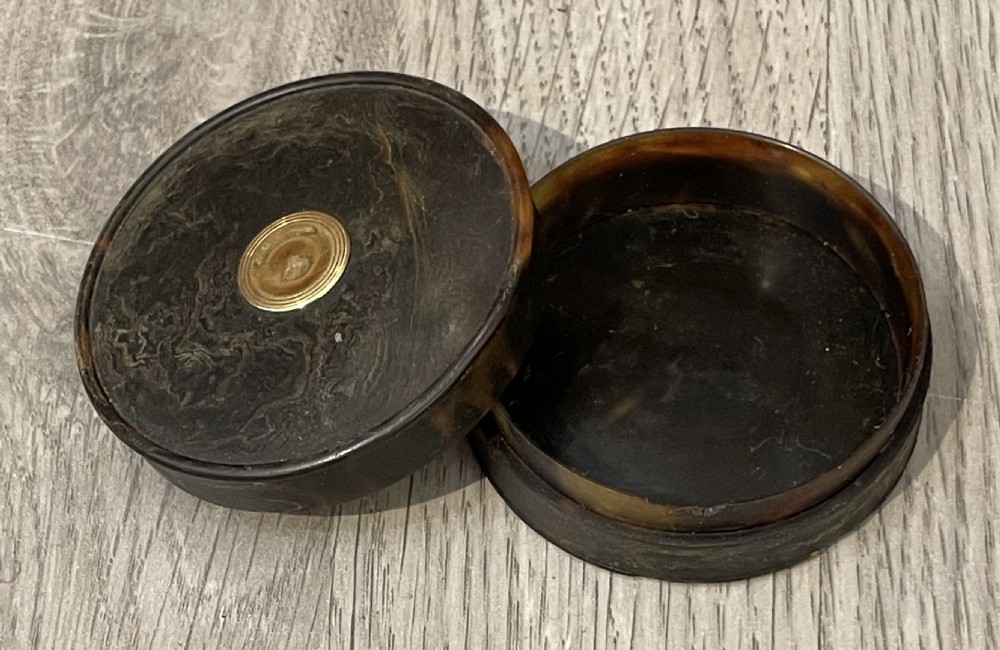 A small circular dark brown tortoiseshell snuff box with a central gold medallion inlay. View VI