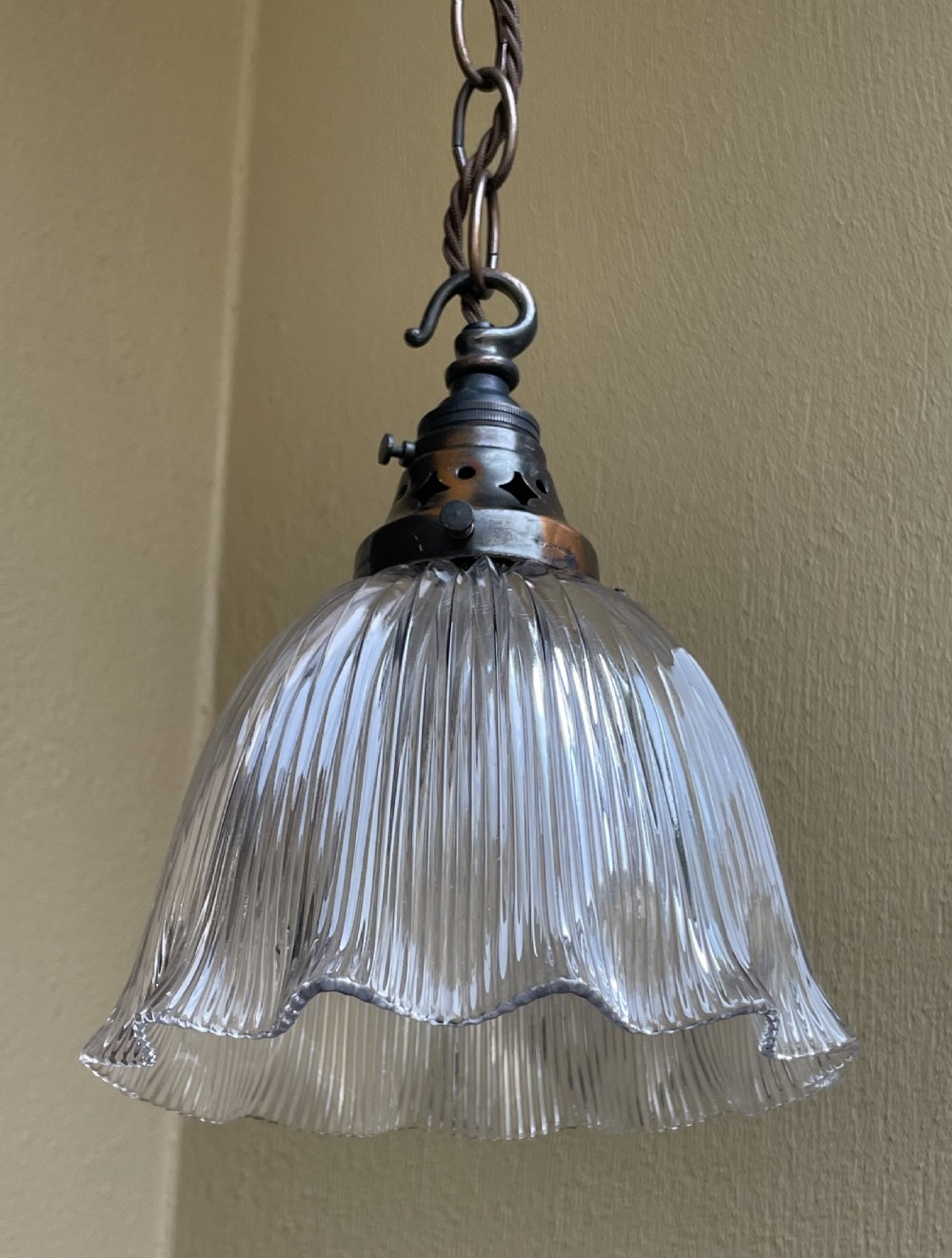 An Edwardian pendant light featuring a clear prismatic fluted glass bell shade suspended from a patinated brass gallery and chain. View II