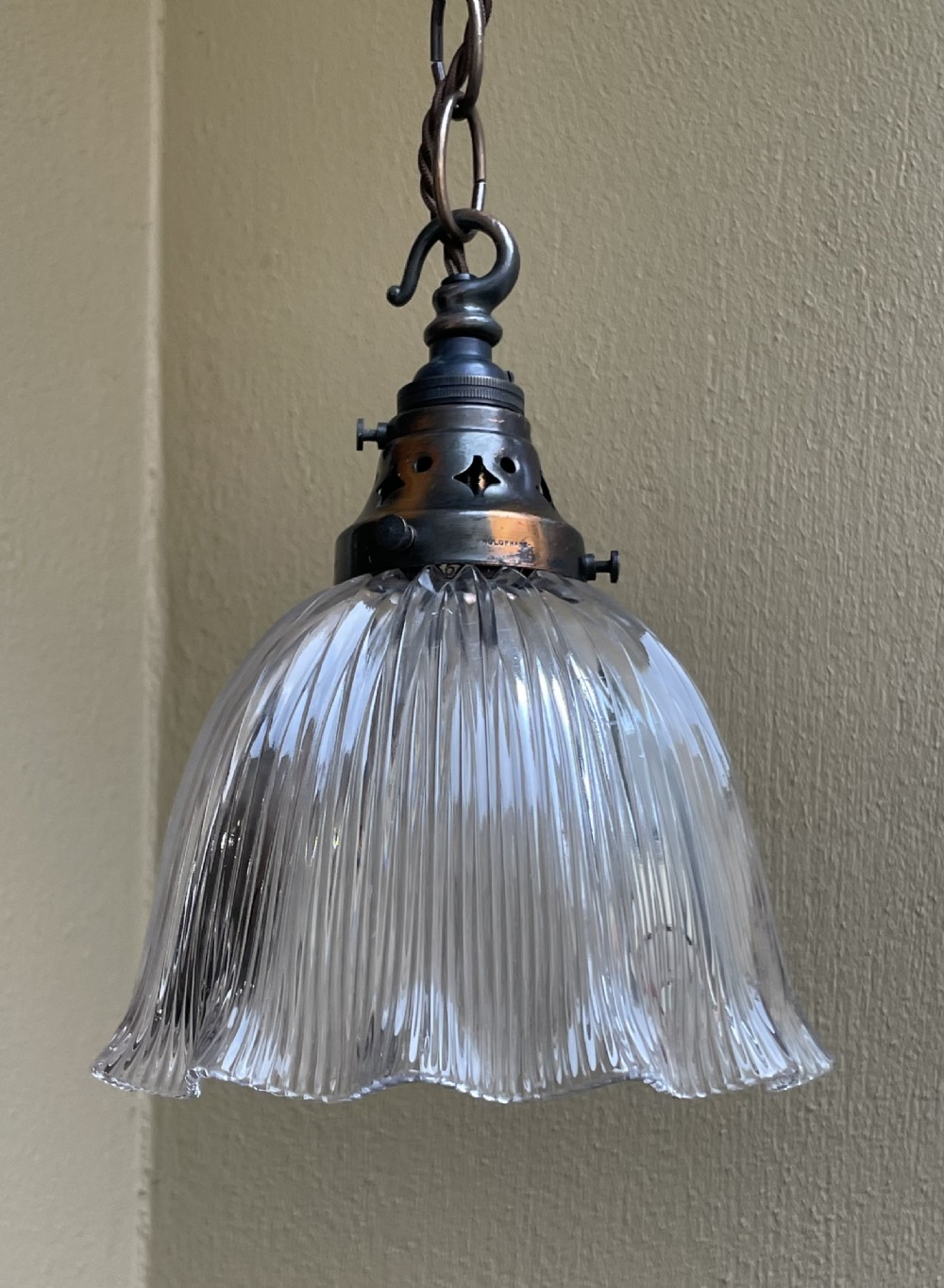 An Edwardian pendant light featuring a clear prismatic fluted glass bell shade suspended from a patinated brass gallery and chain. View V