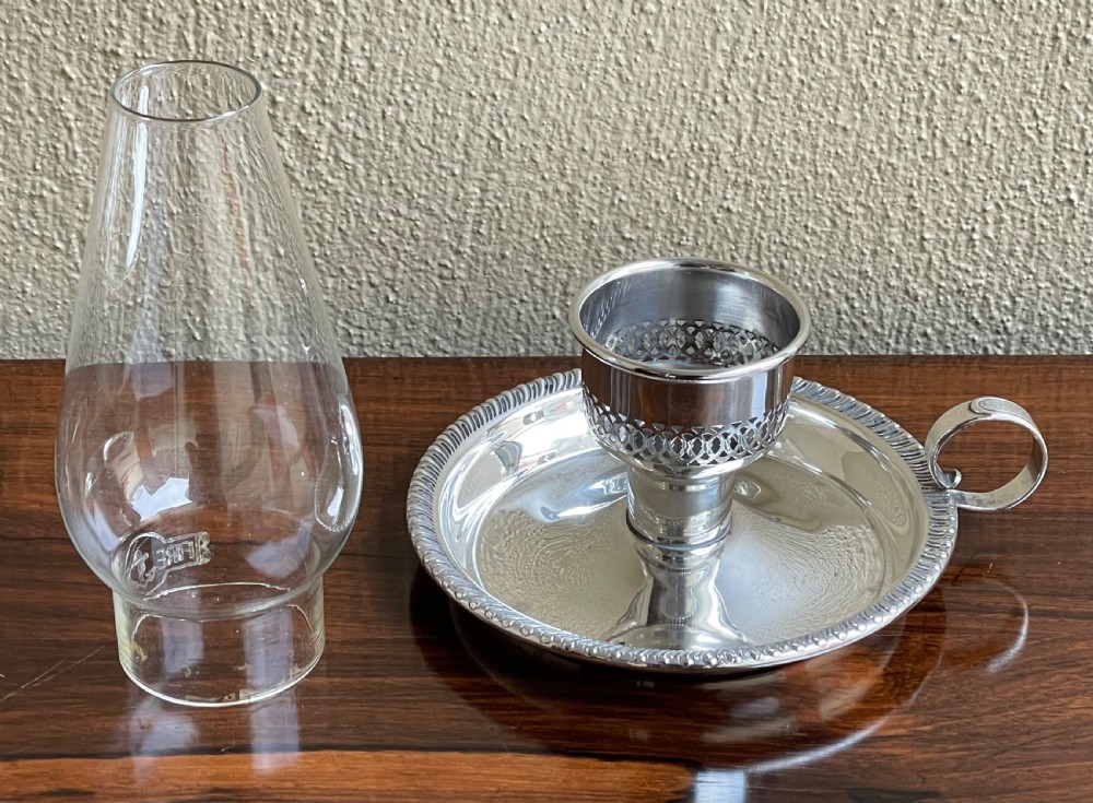 An Art Deco silver chamberstick featuring a tray base with a beaded rim, a pierced candle socket, a side ring handle, and a tall clear glass hurricane shade. View III