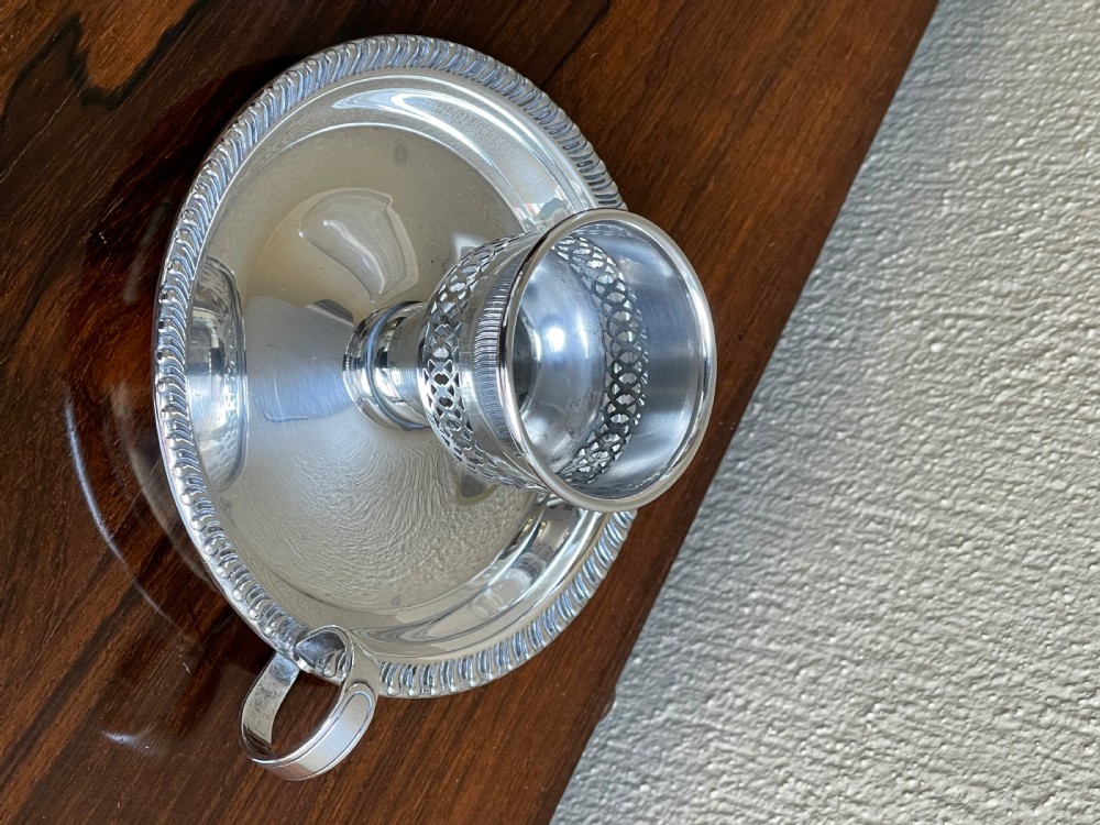An Art Deco silver chamberstick featuring a tray base with a beaded rim, a pierced candle socket, a side ring handle, and a tall clear glass hurricane shade. View IV