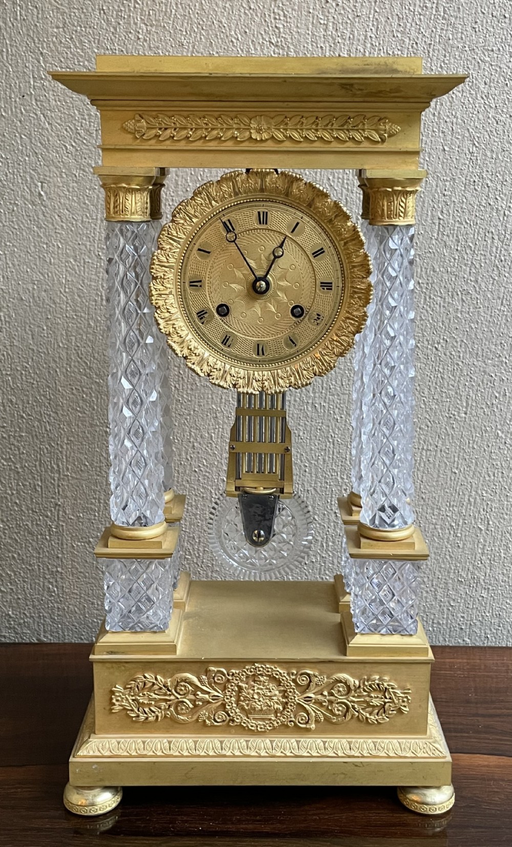 A French Charles X portico mantel clock designed with four diamond-cut crystal columns, gilt ormolu mounts, an engine-turned circular dial, and a pendulum.