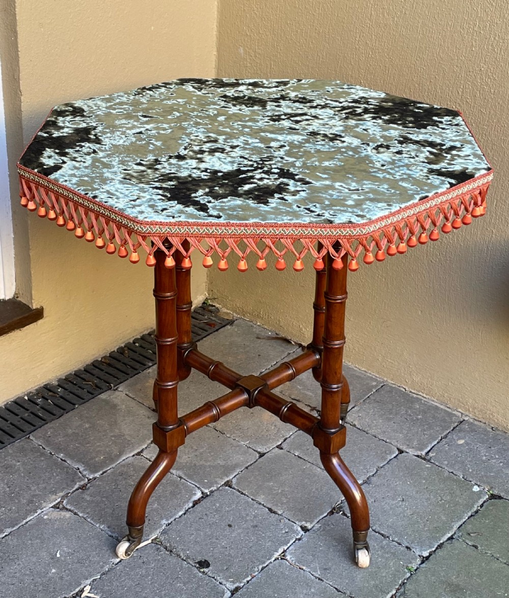 A Victorian octagonal gypsy table with a patterned velvet top, terracotta fringe trim, turned faux-bamboo legs, and ceramic castors.