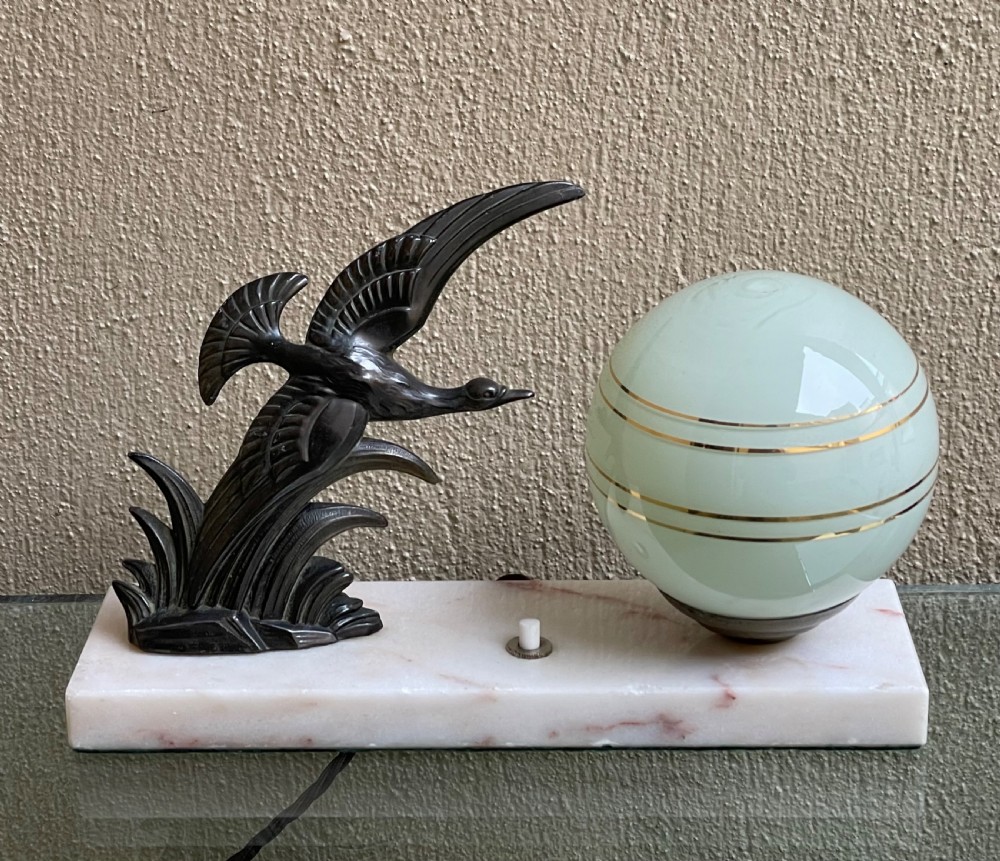 A French Art Deco table lamp featuring a dark patinated spelter bird figure and a frosted green glass globe shade mounted on a rectangular pink marble base.