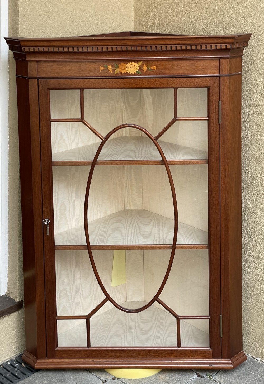 A Georgian style mahogany corner cabinet featuring an astragal glazed door with an oval geometric motif and floral marquetry frieze.