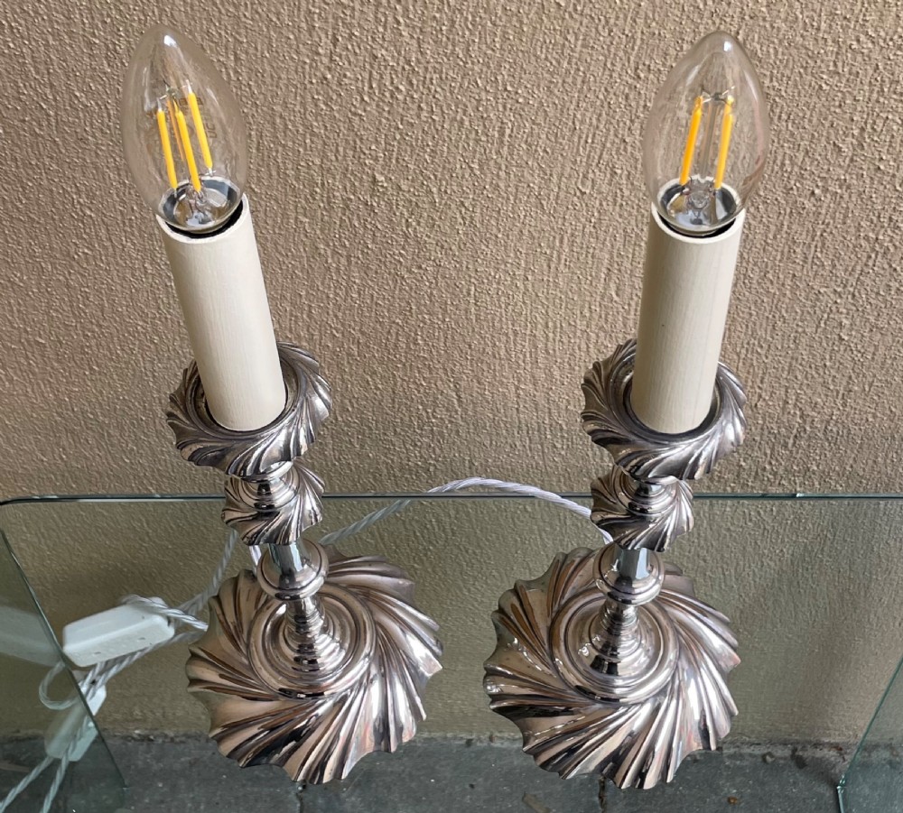 A pair of Victorian silver-plated electric candlestick lamps featuring swirl fluted bases and shafts fitted with cream candle sleeves. View V