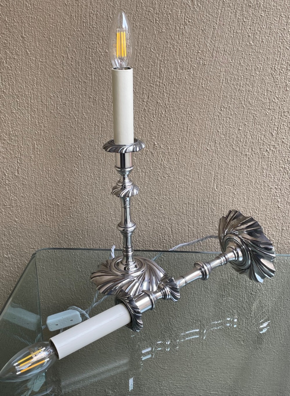 A pair of Victorian silver-plated electric candlestick lamps featuring swirl fluted bases and shafts fitted with cream candle sleeves. View VI