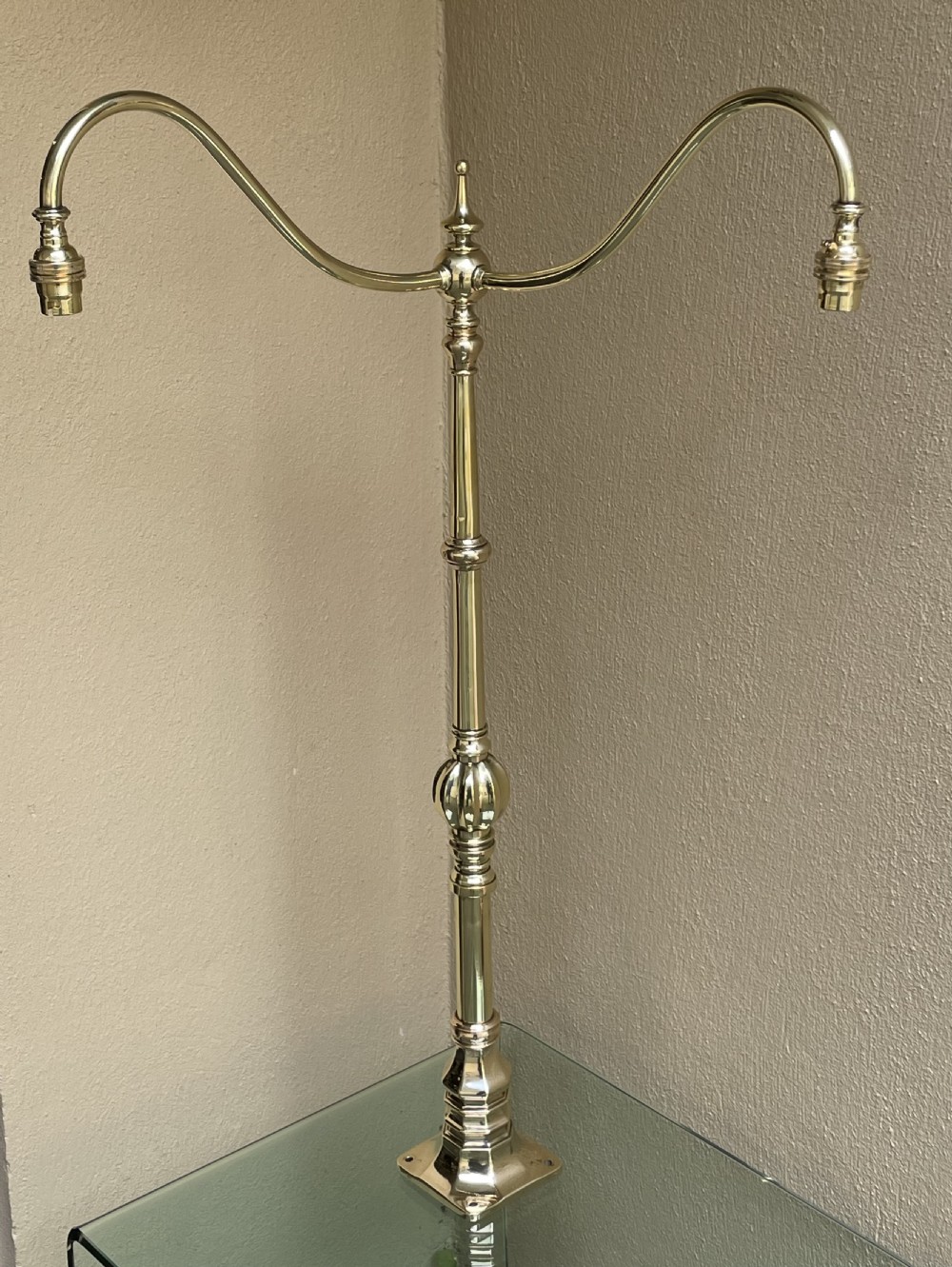 A tall, polished Edwardian brass newel post lamp featuring a central turned stem, two curving branches with lamp holders, and a square mounting base.