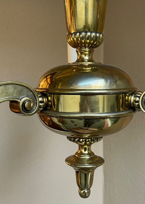 An early 20th-century cast brass chandelier with a central baluster stem, three scrolling arms holding white candle sleeves, and a hanging chain loop. View V
