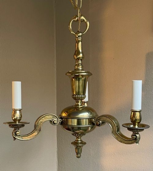 An early 20th-century cast brass chandelier with a central baluster stem, three scrolling arms holding white candle sleeves, and a hanging chain loop. View VI