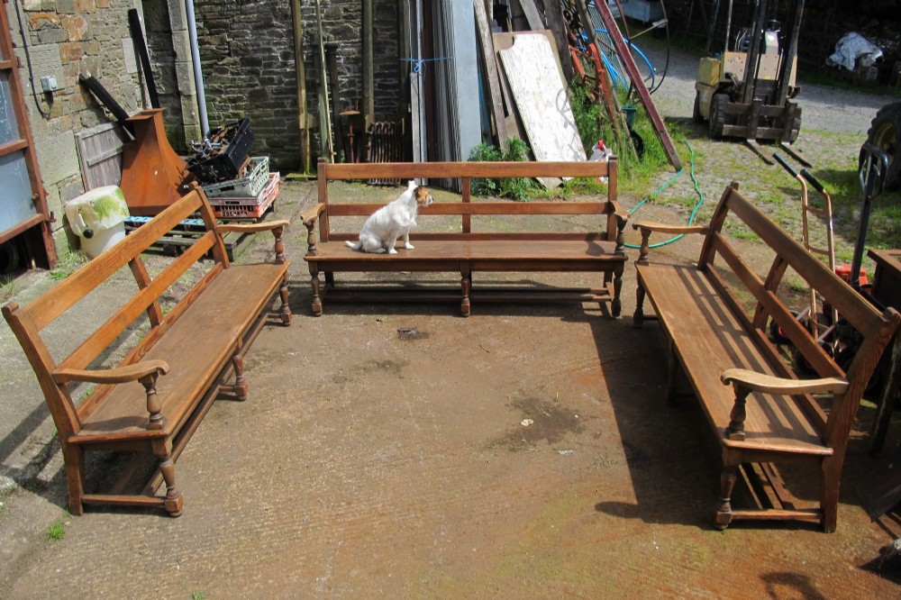 A long Victorian wooden waiting room bench featuring turned front legs, sculpted armrests, and an open rail back.