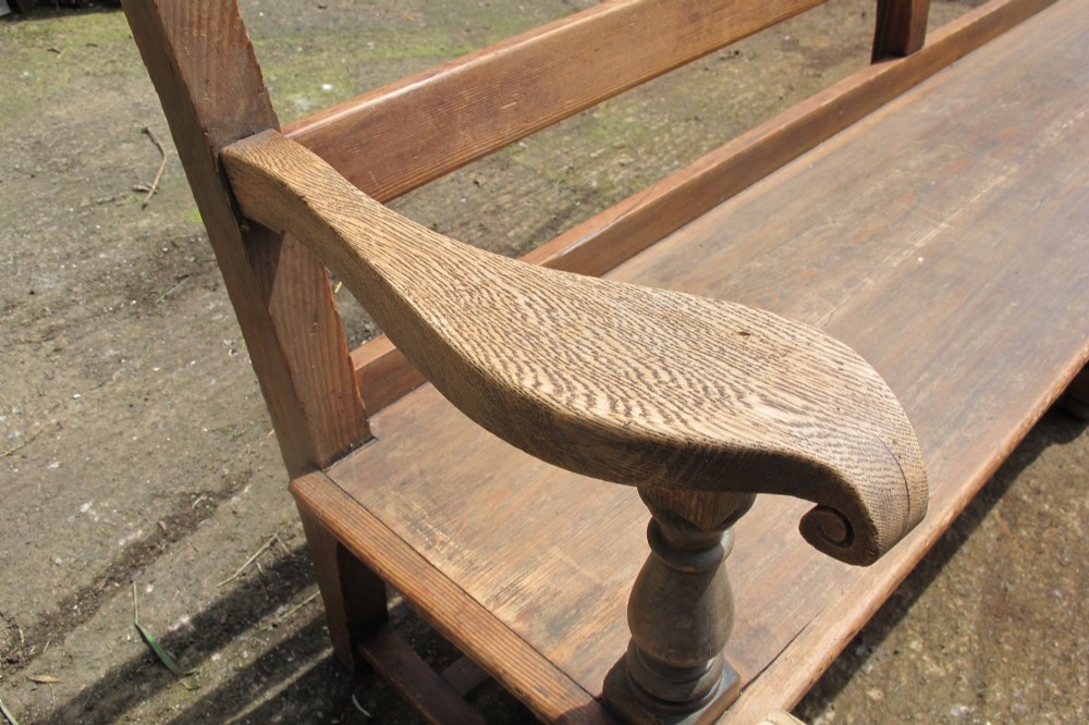 A long Victorian wooden waiting room bench featuring turned front legs, sculpted armrests, and an open rail back. View III