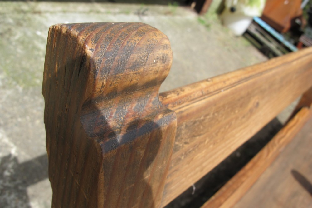 A long Victorian wooden waiting room bench featuring turned front legs, sculpted armrests, and an open rail back. View V