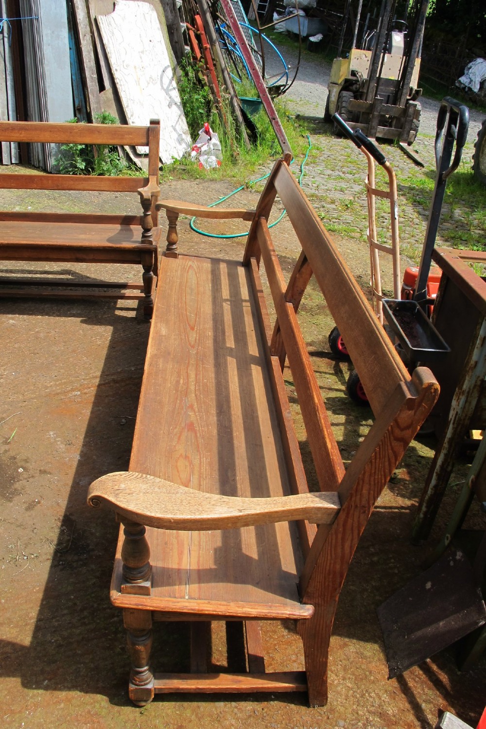 A long Victorian wooden waiting room bench featuring turned front legs, sculpted armrests, and an open rail back. View VI