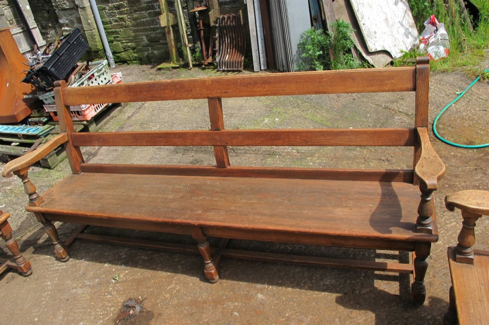 A long Victorian wooden waiting room bench featuring turned front legs, sculpted armrests, and an open rail back. View VII