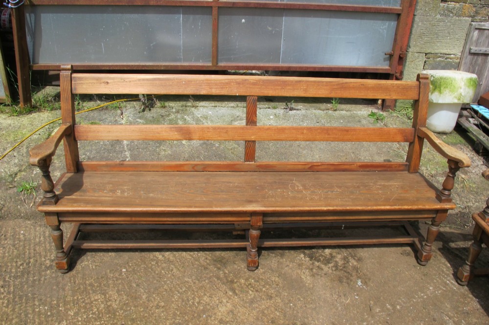 A long Victorian wooden waiting room bench featuring turned front legs, sculpted armrests, and an open rail back. View VIII