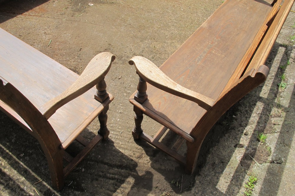 A long Victorian wooden waiting room bench featuring turned front legs, sculpted armrests, and an open rail back. View X