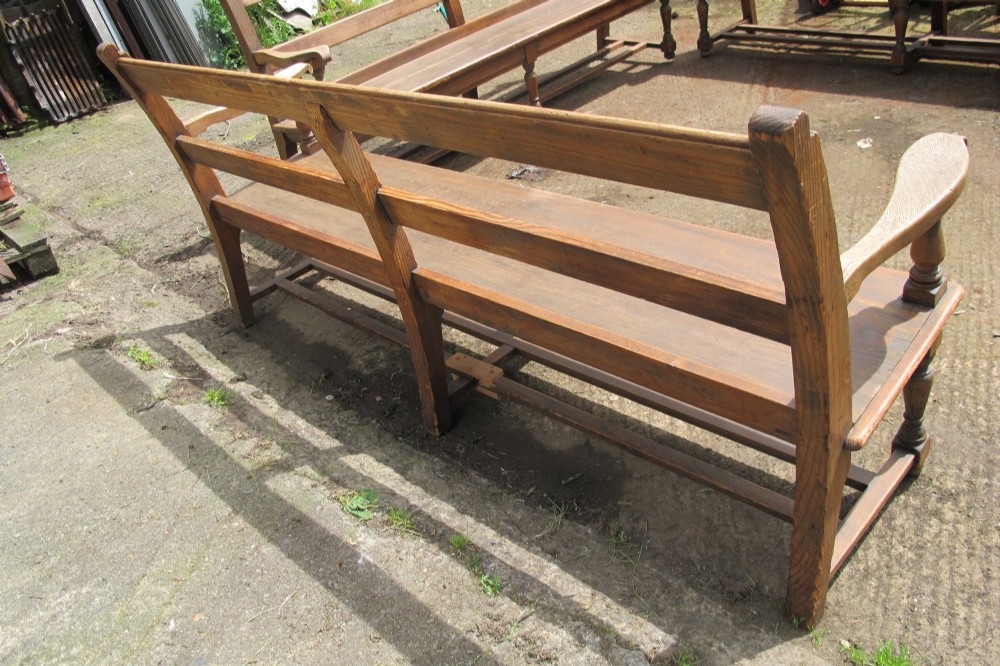 A long Victorian wooden waiting room bench featuring turned front legs, sculpted armrests, and an open rail back. View XII