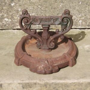 A Victorian cast iron boot scraper featuring scrollwork side handles and a central scraping blade set within a circular catching tray.