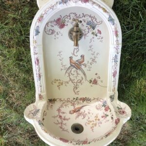 A late Victorian cream glazed ceramic wall-mounted fountain basin with floral transferware, bird decoration, and a brass tap.