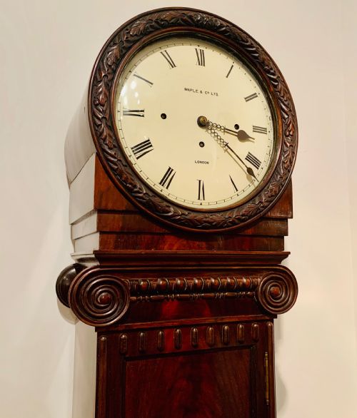 fig 2. An Edwardian dark mahogany longcase clock featuring a circular white dial with Roman numerals, carved ionic capital columns, and a panelled base.