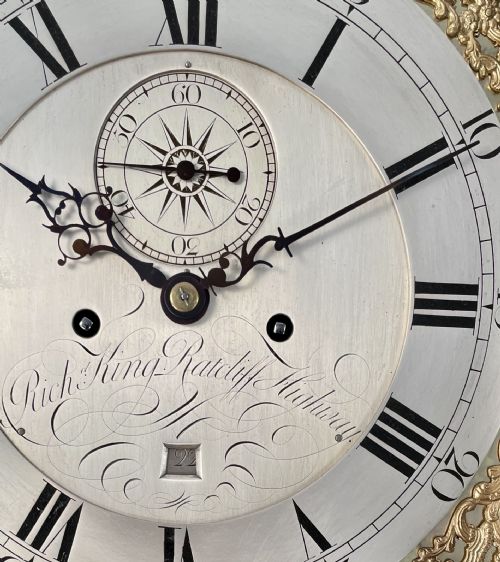 fig 2. A Georgian dark flame mahogany longcase clock featuring an arched hood with reeded brass-capped columns and an engraved brass dial.