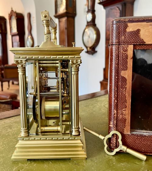 fig 1. An antique brass French carriage clock with fluted corner columns, Corinthian capitals, a white enamel dial with Roman numerals, and a top handle.
