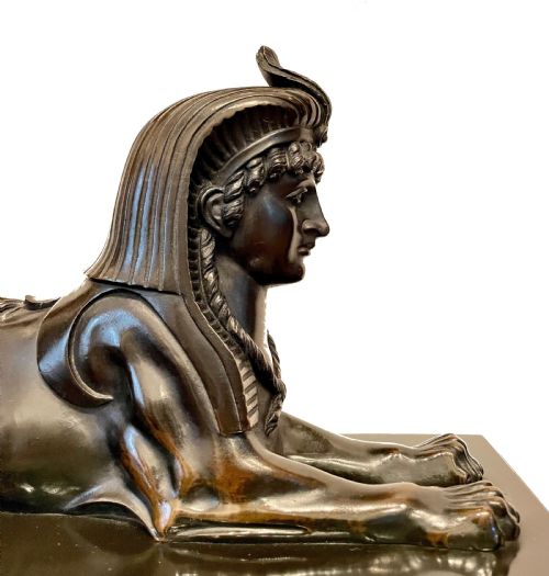 fig 2. An Egyptian Revival mantel clock constructed from black slate and red marble, topped with a reclining bronze sphinx and flanked by two seated sphinx figures.