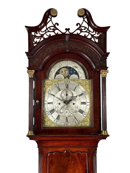 fig 1. An antique Georgian mahogany longcase clock featuring a swan-neck pediment with pierced fretwork, a moonphase arch dial, and brass-mounted corner columns.