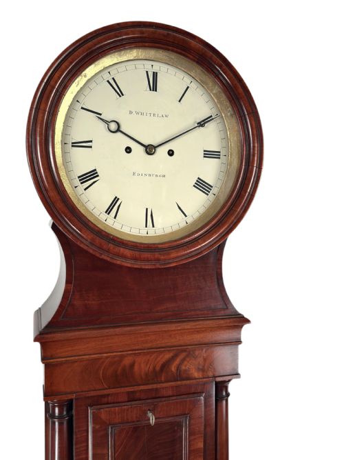 fig 1. A Scottish Regency flame mahogany longcase clock featuring a circular brass-rimmed dial with Roman numerals and a veneered trunk on bracket feet.