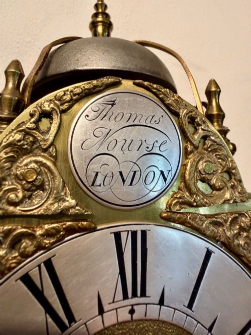 fig 1. An antique miniature brass hook and spike wall clock with an engraved silvered chapter ring, ornate spandrels, and a top bell assembly.